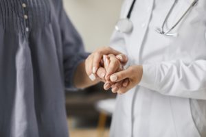 Mãos de médica segurando as mãos do paciente
